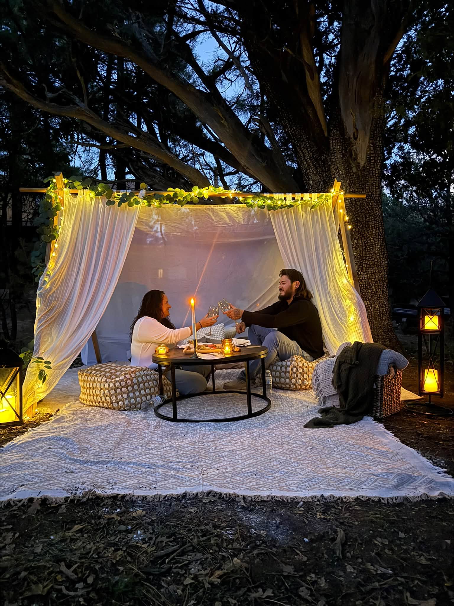 A candlelit private picnic setting beneath a large pine tree